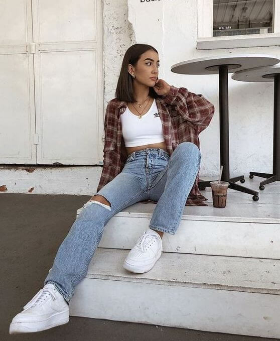 Foto de mujer usando camisa leñadora grande con blusa blanca ajustada al cuerpo, jean azul roto en las rodillas y tennis blancos